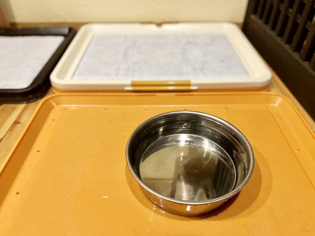 犬用のトイレの前に犬用のステンレスのご飯入れが置かれている写真